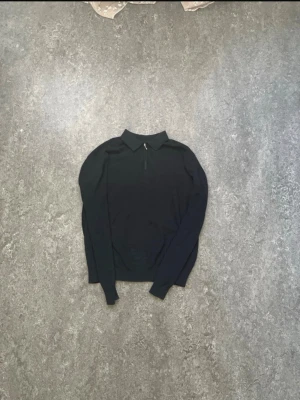 Svart långärmad tröja med krage - Stilren svart långärmad tröja med klassisk krage och dragkedja framtill. Perfekt för dig som gillar en enkel men snygg look. Tröjan har en smal passform och är tillverkad i ett mjukt material som känns skönt mot huden.
