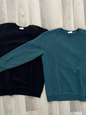 Två crewneck sweatshirts i bomull - Säljer två stilrena crewneck sweatshirts utan huva, en i svart och en i mörkgrönt. Båda har klassisk rund halsringning och ribbade muddar vid ärmslut och nederkant. Perfekta till vardags och gjorda i mjuk bomull för skön känsla.