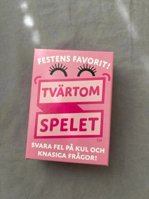 Tvärtom Spelet sällskapsspel - Roligt sällskapsspel i kortformat där du ska svara fel på knasiga frågor. Lådan är rosa med vit och mörkrosa text och innehåller flera kort med frågor. Perfekt för spelkvällar med vänner eller familj.