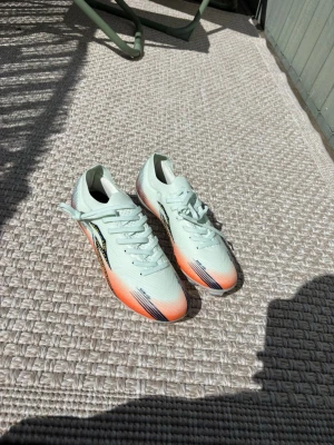 Mintgröna Puma sneakers med orange detaljer - Fräscha sneakers från Puma i mintgrönt meshmaterial med coola orange och svarta detaljer på tån och sidorna. Lätta och sportiga med klassisk snörning och låg profil. Perfekta för dig som vill sticka ut med stilrena men ändå färgstarka skor.