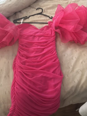 Chockrosa puffärmad klänning - Superfin chockrosa klänning med stora puffärmar och draperad design. Klänningen har en figurnära passform och är gjord i ett tunt, transparent tyg med volym. Perfekt för dig som vill sticka ut och älskar färg och statement-ärmar.