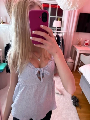 Ljuslila linnetopp med knyt - Supersöt ljuslila linnetopp med knyt framtill och smala axelband. Toppen har en lätt strukturerad yta och v-ringning, perfekt för varma dagar. Sitter löst och bekvämt över kroppen.