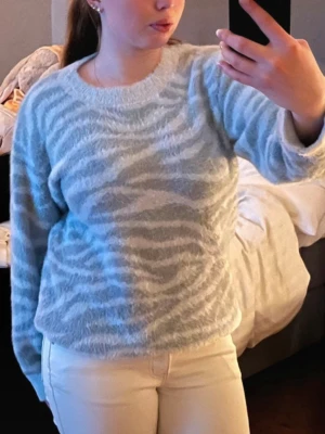 Ljusblå zebramönstrad stickad tröja - Mysig stickad tröja i ljusblått med zebramönster i vitt. Tröjan har rund halsringning, långa ärmar och är fluffig i materialet. Perfekt för dig som gillar djurmönster och vill ha en trendig look. Super skön och sitter fint på! 