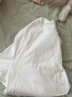 Vit basic t-shirt i bomull - En klassisk vit t-shirt med rund hals och korta ärmar. Perfekt att matcha med jeans eller shorts för en clean och enkel look. Tillverkad i mjuk bomull som känns skön mot huden.