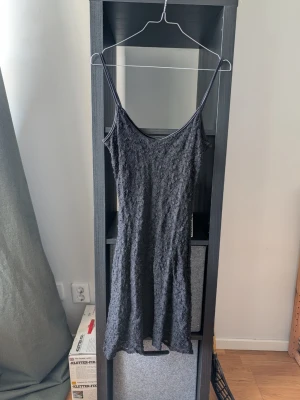 Svart klänning med spets från Impuls - Säljer en svart klänning från Impuls i storlek S. Klänningen har smala axelband, ärmlös design och är täckt av ett fint spetsliknande material. Passformen är figurnära och längden är kort, perfekt för dig som gillar en enkel men elegant look.