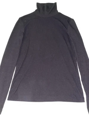 Svart polotröja i ribbad bomull - Klassisk svart polotröja med ribbad struktur och lång ärm. Tillverkad i mjuk bomull som känns skön mot huden. Perfekt basplagg med hög krage som ger en stilren look. Enkel att matcha med olika outfits.