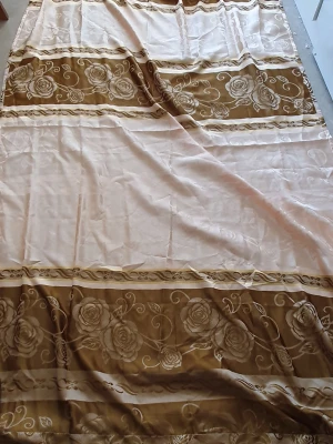 Gardin - Stor gardin i beige och brunt med dekorativa rosor och blommönster i breda ränder. Gardinens material känns mjukt och har fransar längs ena kanten.