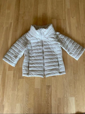 Vit pufferjacka från Lemonada - Snygg vit pufferjacka från Lemonada med horisontella sömmar och hög krage. Jackan har dragkedja framtill och är tillverkad i ett glansigt, quiltat material som håller värmen under kalla dagar. Perfekt för dig som vill ha en stilren vinterlook.