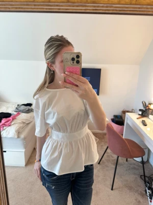 Vit peplumblus med korta ärmar - Säljer en vit peplumblus med rund hals och korta ärmar. Blusen har en markerad midja och ett lätt, luftigt material som ger en snygg siluett. Perfekt att matcha med jeans eller kjol för en trendig look.