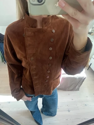 Brun mockajacka - Brun mockajacka med dubbelknäppning och snygg krage. Perfekt som vårjacka! Jackan är i äkta läder satt det är bra kvalité. Storleken är S/M