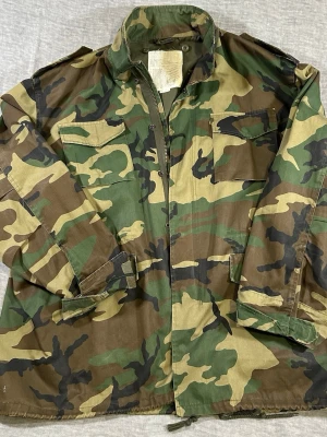 Oversized Woodland Camo Military Field Jacket XXL Rothco Utility - Rothco Ultra Force woodland camo field jacket. Classic military style with four pocket utility design and durable cotton/poly fabric.  Oversized XXL fit – perfect for layering over hoodie or knit.  Shows normal wear with small paint marks on lower back (see photos). Missing detachable hood.  Measurements: S2S 51 cm, P2P 62 cm, Waist 59 cm, Sleeve 68 cm, Length 74 cm.