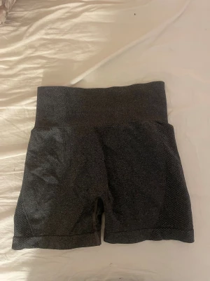 Mörkgrå träningstights shorts - Säljer ett par mörkgrå träningstights shorts med hög midja och meshdetaljer på sidorna. Perfekta för gymmet eller löprundan, de är stretchiga och sitter skönt på kroppen.