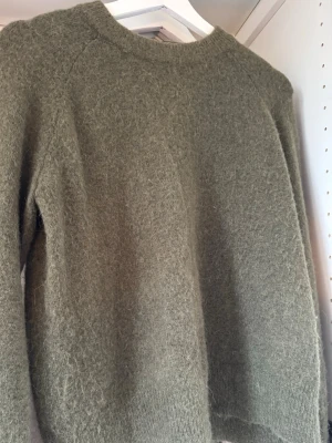Olivgrön stickad tröja från Zara - Mysig olivgrön stickad tröja från Zara med lång ärm och rund hals. Tröjan har en fluffig och mjuk känsla, perfekt för kyliga dagar. Enkel och stilren design som passar till det mesta.