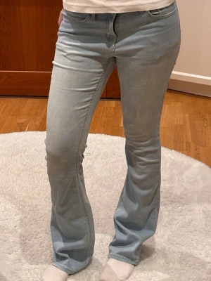 Ljusblå bootcut jeans - Säljer ett par ljusblå bootcut jeans med klassisk femficksmodell och normal/ låg midja. Jeansen har en snygg tvätt och är tillverkade i ett mjukt denimtyg med lite stretch för extra komfort. 