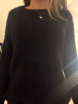 svart  fluffig stickad tröja - Mysig svart stickad tröja med rund hals och lång ärm. Tröjan har en fluffig, mjuk struktur som ger en avslappnad och trendig look. Perfekt att matcha med jeans eller kjol för en enkel men snygg outfit.