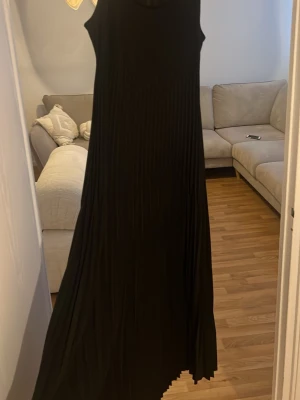 Midjad Svart långklänning i plisserad modell - Säljer en svart långklänning med ärmlös design och plisserad kjol. Klänningen har en midjad passform och flowy nertill. Jätte fin material, skön och mycket br kvalite. Perfekt för en sommarkväll. Storlek XS som passar även bra för S och kanske M då klänningen är stretchig. 