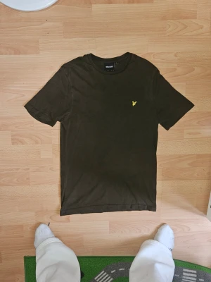 Mörkgrön t-shirt från Lyle & Scott - En stilren mörkgrön t-shirt från Lyle & Scott med klassisk passform och korta ärmar. T-shirten har en rund halsringning och den ikoniska gula logon broderad på bröstet. Perfekt till jeans eller shorts för en enkel och snygg look.