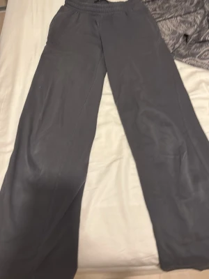 Mörkgrå mjukisbyxor med resårmidja - Säljer ett par mörkgrå mjukisbyxor med bred resår i midjan och raka ben. Byxorna har en enkel och clean look utan synliga loggor eller detaljer. Perfekta för chill dagar hemma eller när du vill ha det bekvämt. Materialet känns mjukt och skönt mot huden.