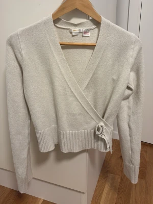 Vit omlottkofta - Säljer en stilren vit stickad omlottkofta från Gina Tricot. Koftan har långa ärmar, ribbade muddar och knytdetalj i sidan. Perfekt att slänga över en topp för en snygg lager-på-lager-look. Passar även storlek xs och s. Säljs pga att den inte används längre. Skriv gärna ifall ni skulle vilja ha fler bilder. Pris går att diskutera.