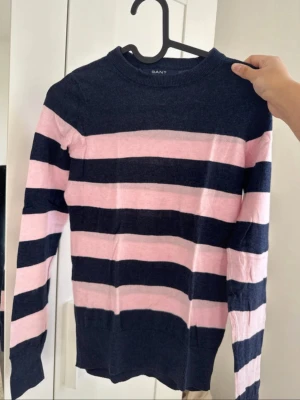 Randig stickad tröja från GANT - Säljer en snygg stickad tröja från GANT med breda marinblå och ljusrosa ränder. 