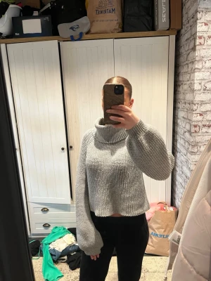 Grå croppad polotröja stickad - Säljer en grå, croppad stickad polotröja med breda ärmar och ribbad struktur. Tröjan har en hög, lös polokrage och avslappnad passform som ger en trendig look. Perfekt för dig som gillar mysiga och stilrena plagg.