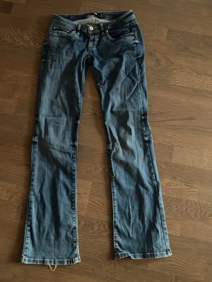 Blå bootcut jeans från LTB - Säljer ett par blå bootcut jeans från LTB med klassisk femficksdesign och snygga detaljer vid fickorna. Jeansen har en knapp och dragkedja framtill samt bälteshällor. Materialet är denim och passformen är något utsvängd nedtill.