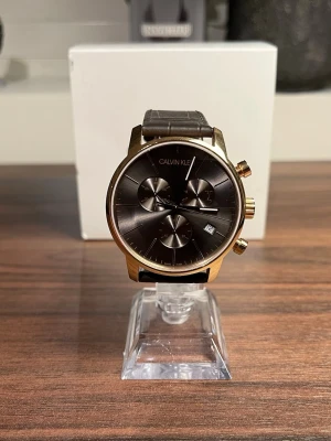 Clavin klein herrklocka - Superfin, i princip helt oanvänd klocka från calvin klein säljes. Inga synliga repor på glaset. Fint brunt armband, stilren case i guld och urtavla i brunt. Modellnummer:k2g276. Nypris: +4000kr, jag säljer den för endast 400kr med helt nytt batteri! Klocklåda ingår, men lite trasig i gångjärnen. 