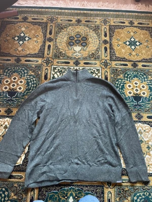 Grå stickad tröja från Eddie Bauer - Mysig grå stickad tröja från Eddie Bauer med halv dragkedja och hög krage. Tröjan har långa ärmar och ribbstickade muddar vid ärmslut och nederkant. Perfekt för lager-på-lager och chill dagar.