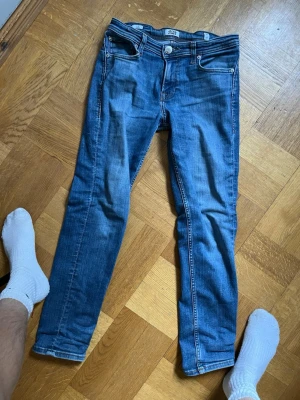 Blå slim fit jeans från H&M - Snygga blå slim fit jeans från H&M med klassisk femficksdesign och dragkedjegylf. Jeansen har en lätt tvättad look och smal passform som sitter tajt längs benen. Perfekta för en trendig och avslappnad stil.