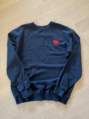Mörkblå sweatshirt från Comme des Garçons (beskrivning) - Mörkblå sweatshirt med rund hals och ribbade muddar från Comme des Garçons Play. Tröjan har det ikoniska röda hjärtat med ögon broderat på bröstet. Perfekt för en stilren och trendig look. säljer gärna med instabox!!