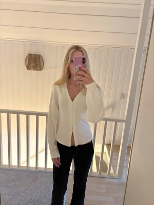 Vit cardigan från Nelly - Snygg vit cardigan från Nelly med v-ringning och knäppning framtill. Tröjan har långa ärmar och en rak passform som passar perfekt till både jeans och kjol. Tillverkad i mjukt material som känns skönt mot huden.