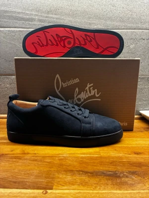 Blåa sneakers från Christian Louboutin - Snygga blåa sneakers från Christian Louboutin med klassisk röd sula och diskret logga. Skorna har en låg profil, rund tå och är tillverkade i ett lyxigt material med svarta skosnören. Perfekt för dig som vill ha en stilren och exklusiv look. 