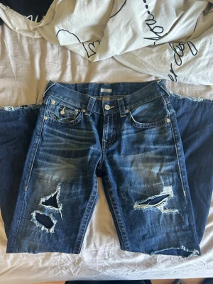 Unika bootcut true religion jeans med hål - Supercoola one of a kind true religion bootcut jeans! Så otroligt coola & sällsynta men tyvärr för små för mig:( Midja 40cm & innerbenslängd 80cm! I deras Billy relaxed bootcut modell!