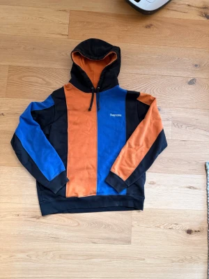 Supreme Hoodie - Säljer en hoodie från Supreme med färgblock i svart, orange och blå.
