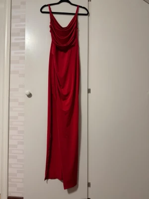 Festklänning - Snygg röd långklänning med draperad urringning framtill och slits vid benet. Klänningen har en elegant, figurnära passform. Perfekt till bal eller bröllop. Endast använd en gång.