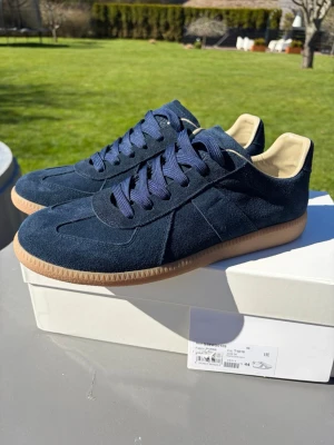 Mörkblå sneakers från Maison Margiela - Stilrena sneakers i mörkblå mocka från Maison Margiela med klassisk gummisula.   Nyligen inköpta men var för små! Aldrig använda. (Små i storleken) Har storlek 44 i vanliga fall men med dessa kan man gå upp 1-2 storleker. 