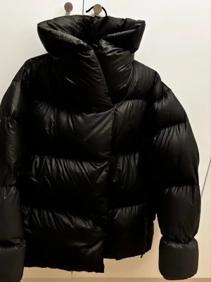 Filippa K Soft Sport svart dunjacka, storlek L. SLUTSÅLD FAVORIT! - Svart dunjacka från Filippa K Soft Sport. Jackan har en stor härlig krage och en avslappnad passform. Den försluts med tryckknappar. Superfin favorit! I fint anv skick! Dyr i inköp! Passa på!