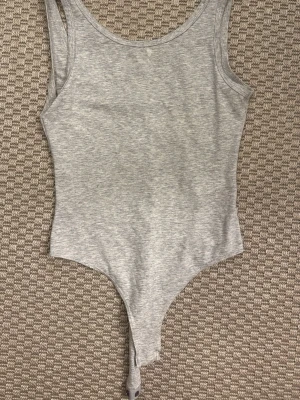 Grå ärmlös body i bomull - En enkel och stilren grå body med ärmlös design och rund halsringning. Tillverkad i mjukt bomullsmaterial som känns skönt mot huden. Perfekt att bära under andra plagg eller som den är.