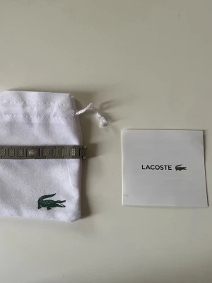Lacoste Armband - Snyggt armband i silverfärgad metall från Lacoste med rektangulära länkar och diskret Lacoste-logga. Armbandet har en stilren och modern design som passar perfekt till din outfit. Levereras med originalpåse och ask. Snabb Levernas 🚚 