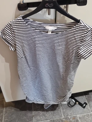 Klassiskt randig mammatopp – H&M Mama (Large) - Håll stilen genom hela graviditeten med den här tidlösa och bekväma bastoppen! Den har en snygg marinblå och vit randig design som passar till allt. Toppen har smarta rynkdetaljer i sidorna som ger gott om plats för den växande magen och skapar en smickrande silhuett. ✨  Gjord i en mjuk och stretchig trikåkvalitet som andas, vilket gör den till en favorit i vardagsgarderoben!  