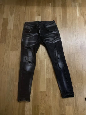 Svarta  jeans med slitningar - Säljer ett par svarta  jeans från desqured  med coola slitningar och blekta detaljer. Perfekta för en edgy streetstil.