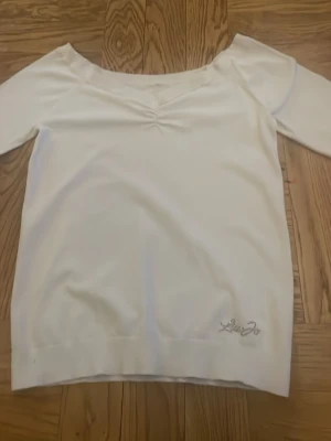 Vit långärmad topp från Liu Jo - Vit långärmad topp från Liu Jo med v-ringning och rynkdetalj framtill. Tröjan har en logga i glitter nertill och är tillverkad i ett stretchigt material. Jag fick denna av min mamma men så jag vet inte hur mycket den har använts men den är lite utstretchad runt kanterna.