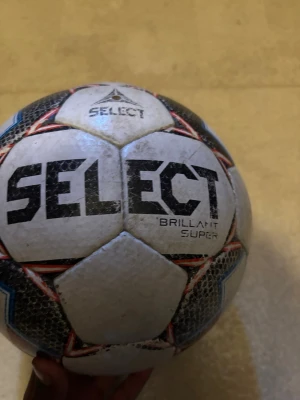 Select Brillant Super fotboll - Säljer en Select Brillant Super fotboll i vitt med svarta, röda och blå detaljer. Klassisk design med hexagonmönster och tydlig logga. Perfekt för matcher eller träning på alla nivåer. Materialet är slitstarkt syntetläder.