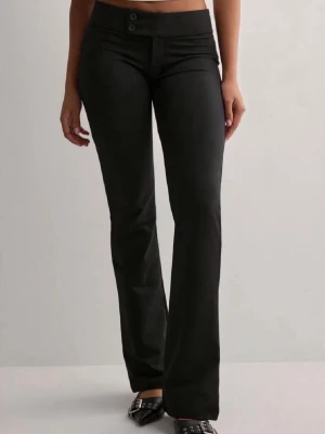 Svarta bootcut byxor med låg midja - Snygga svarta bootcut byxor med låg midja och två knappar framtill. Byxorna har en figurnära passform upptill och utsvängda ben. Perfekta för en trendig och stilren look.