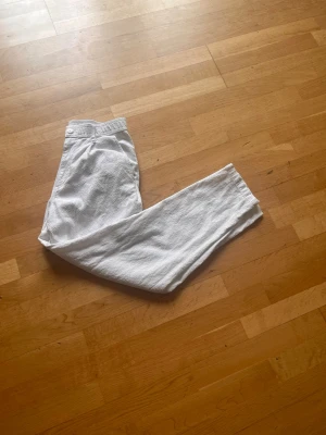 Vita linnebyxor Zara - Snygga vita linnebyxor med rak passform och klassisk midja. Byxorna har knapp och dragkedja framtill samt sidfickor. Perfekta för en avslappnad och stilren look. Materialet är luftigt linne som ger en skön känsla.