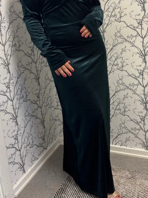 Mörkgrön offshoulder sammetsklänning och balklänning  - (Stl S-M) Elegant lång balklänning i mörkgrön sammet med offshoulder-design och långa ärmar. Klänningen har en mjuk och följsam passform som ger en lyxig känsla. Perfekt för dig som vill sticka ut med en stilren och sofistikerad look.