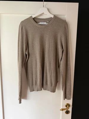 Beige stickad tröja - Snygg beige stickad tröja med rund halsringning och ribbade muddar vid ärmslut och nederkant. Tröjan har en klassisk och stilren design, perfekt att matcha med jeans eller chinos. Materialet känns mjukt och lätt.