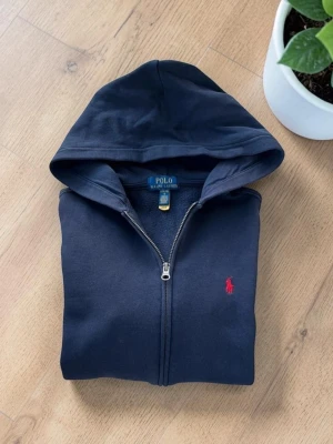 Marinblå Ralph Lauren zip hoodie  - Fint välanvänt skick! Har ett litet hål på ryggen och mudden, annars fin. Passar ca 160 cm Hör av dig vid frågor!