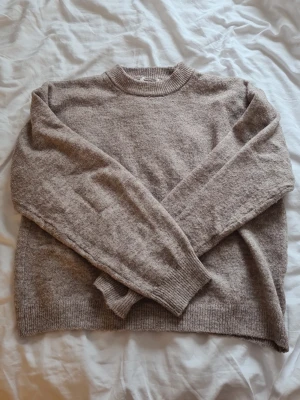 Beige stickad tröja från H&M - Mysig beige stickad tröja med rund hals och långa ärmar. Tröjan har ribbstickade muddar vid ärmslut och nederkant, vilket ger en klassisk och avslappnad look. Perfekt för lager-på-lager och passar till det mesta i garderoben.