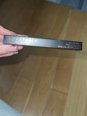 Anastasia Brow Wiz ögonbrynspenna - Slimmad ögonbrynspenna från Anastasia Beverly Hills i svart förpackning med guldtext. Brow Wiz är känd för sin tunna spets som ger naturliga och definierade bryn. Perfekt för att fylla i och forma ögonbrynen med precision.